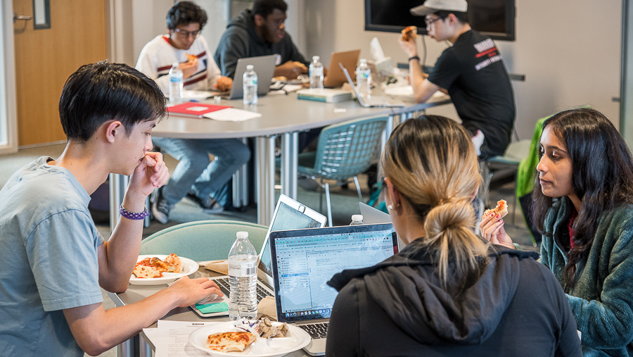 Students eating pizza while working on a laptop